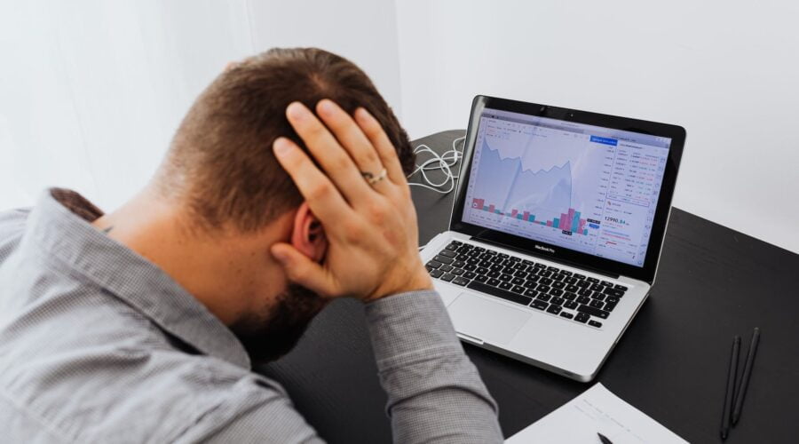 man with laptop on desk terrified by stock market chart