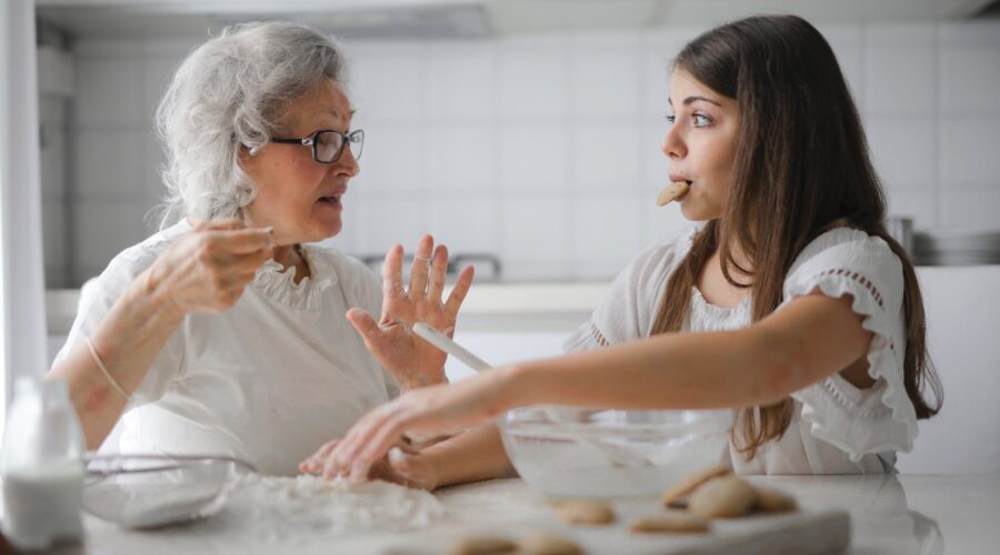 pensive grandmother with granddaughter having interesting conversation while cooking together in light modern kitchen